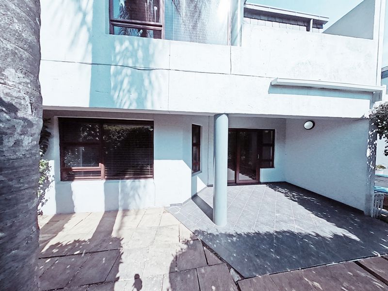 A covered patio area featuring tiled flooring, a structural support column, and sliding glass door access to the interior of the townhouse.