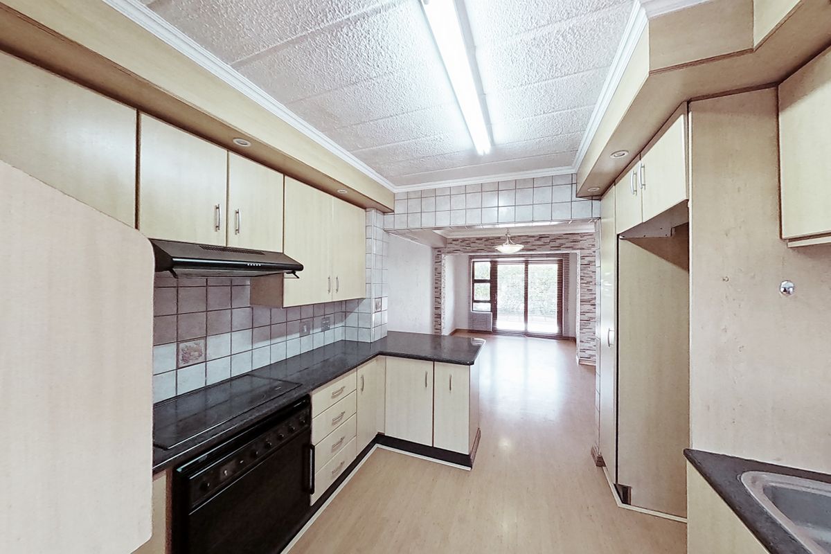 A functional kitchen featuring built-in cabinetry, laminate countertops, an electric stove with extractor fan, and a stainless steel sink, leading into an open living area.