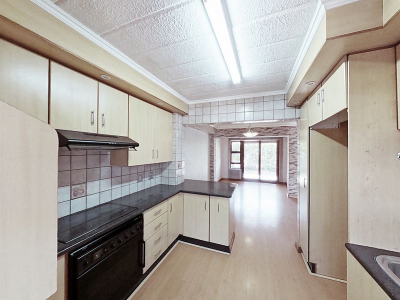 A functional kitchen featuring built-in cabinetry, laminate countertops, an electric stove with extractor fan, and a stainless steel sink, leading into an open living area.