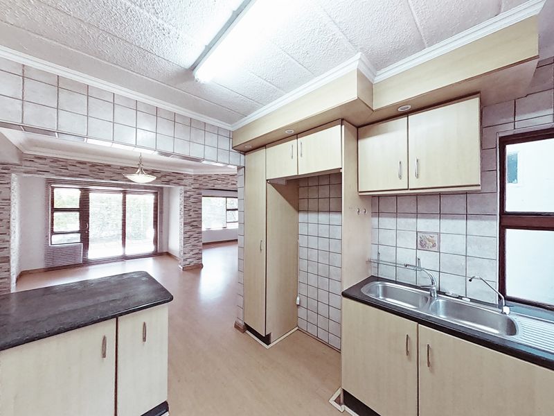 Open plan kitchen and living area featuring laminate flooring, built-in cabinetry, and a double basin sink, offering a functional layout ready for modernization.