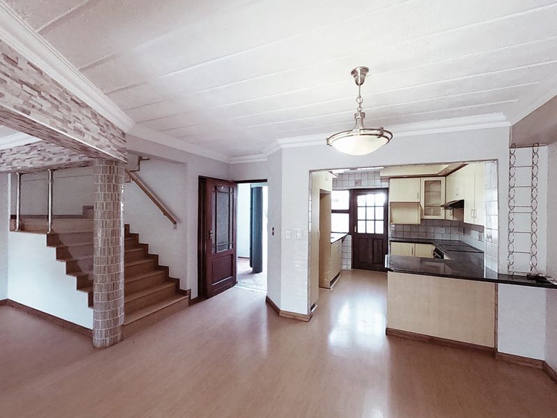 Open-plan living area featuring a staircase, decorative stone pillar, and a functional kitchen with built-in cabinetry and stone countertops.