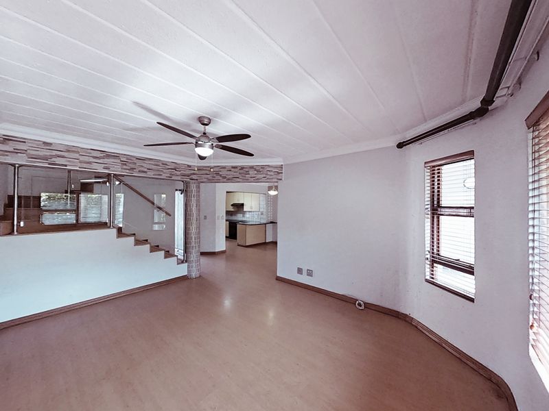 Spacious open-plan living area featuring a staircase with glass balustrade, ceiling fan, and views into the kitchen area.