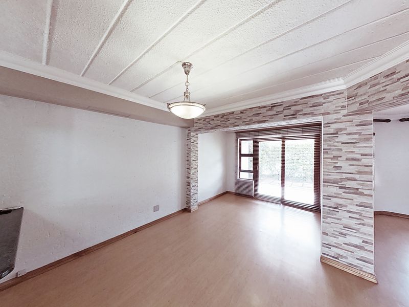 An empty living room featuring laminate flooring, a stone-cladded feature wall, and sliding glass doors providing natural light and garden access.