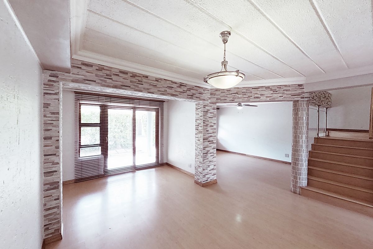 Spacious open-plan living area featuring laminate flooring, stone veneer accents, a staircase, and sliding glass doors leading to the exterior.