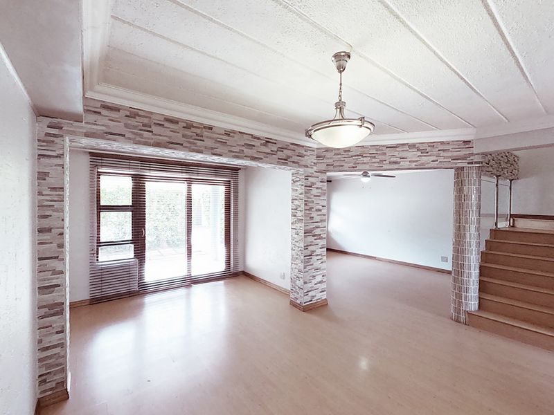 Spacious open-plan living area featuring laminate flooring, stone veneer accents, a staircase, and sliding glass doors leading to the exterior.