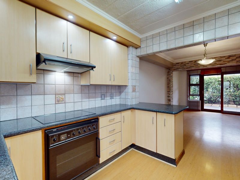 Open-plan kitchen featuring laminate cabinetry, granite countertops, and built-in appliances, flowing into a living area with access to a private outdoor space.