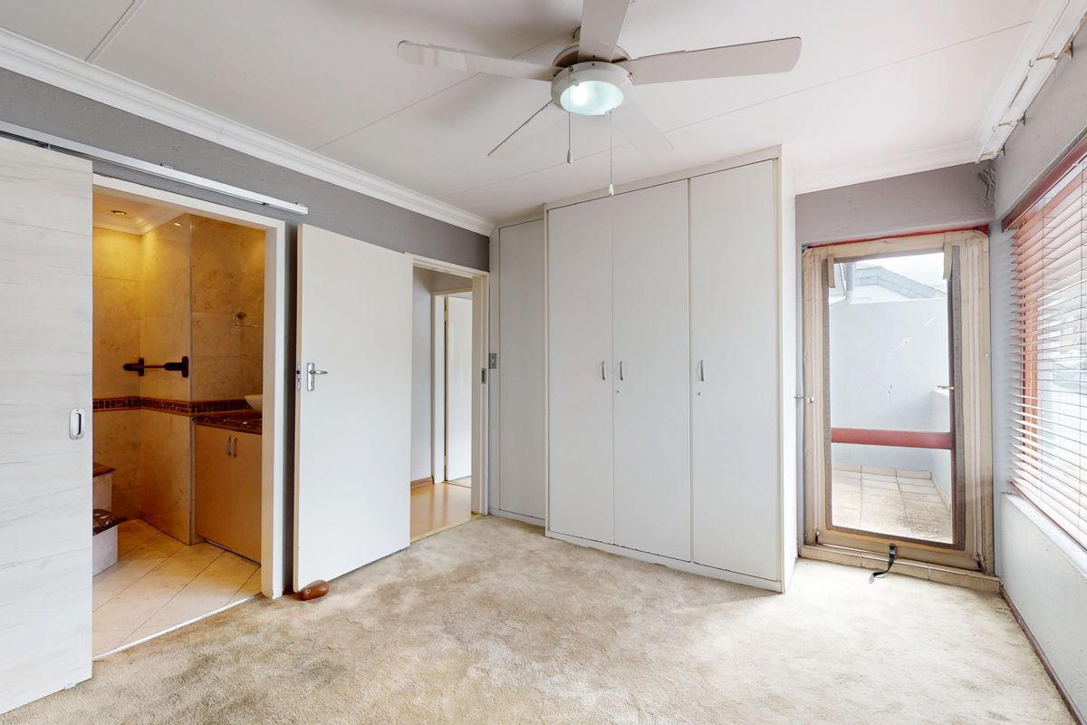 Spacious bedroom featuring built-in cupboards, a ceiling fan, and direct access to an en-suite bathroom, with large windows providing natural light.
