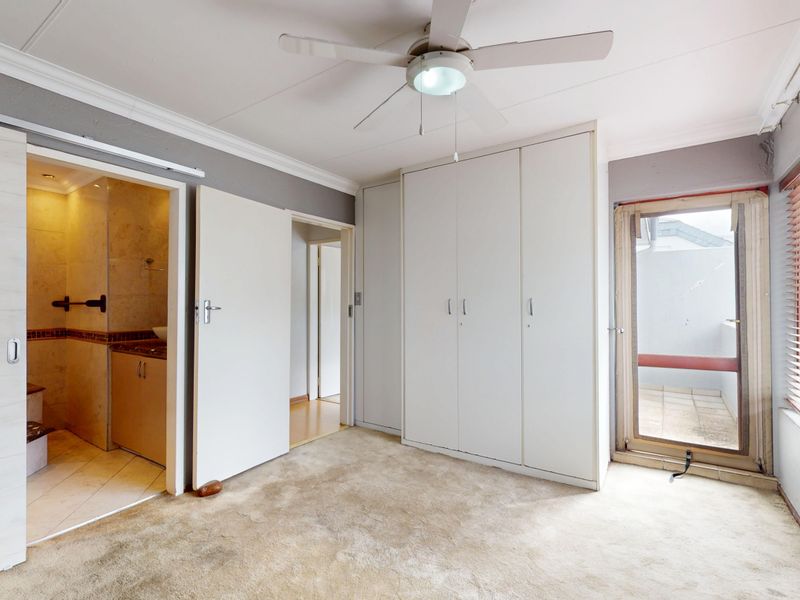 Spacious bedroom featuring built-in cupboards, a ceiling fan, and direct access to an en-suite bathroom, with large windows providing natural light.