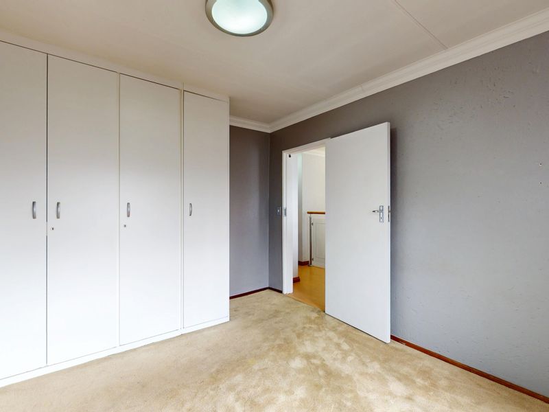 A clean, empty bedroom featuring neutral grey walls, built-in cupboards, and carpeted flooring, offering a versatile space ready for personalization.
