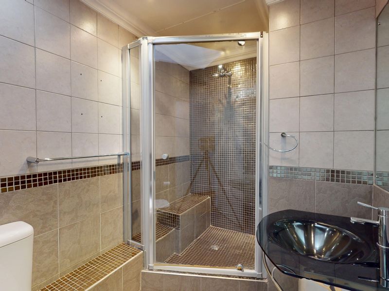 A modern bathroom featuring a glass-enclosed shower with a built-in bench, mosaic tiling, a vessel sink, and neutral ceramic wall finishes.