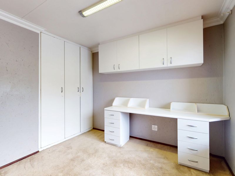 A bedroom featuring built-in cupboards, a fitted desk with overhead storage, and venetian blinds, offering a functional space ready for personalization.