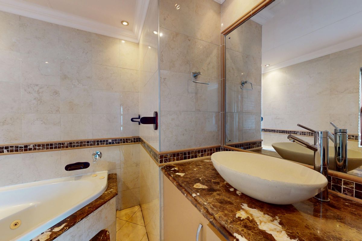 A well-maintained bathroom featuring a built-in bathtub, a stone-topped vanity with a vessel sink, and neutral tiled walls with a decorative mosaic border.