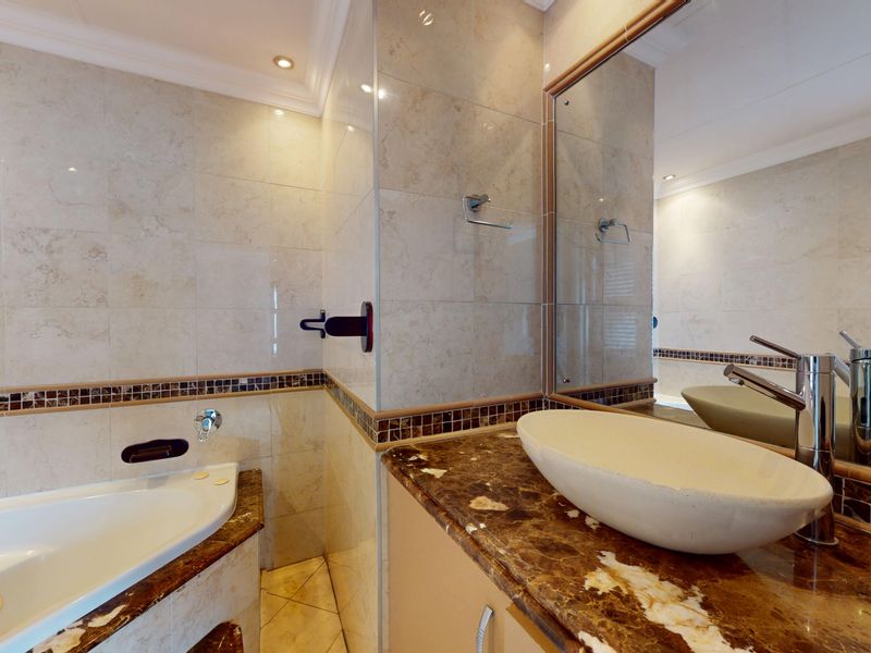 A well-maintained bathroom featuring a built-in bathtub, a stone-topped vanity with a vessel sink, and neutral tiled walls with a decorative mosaic border.