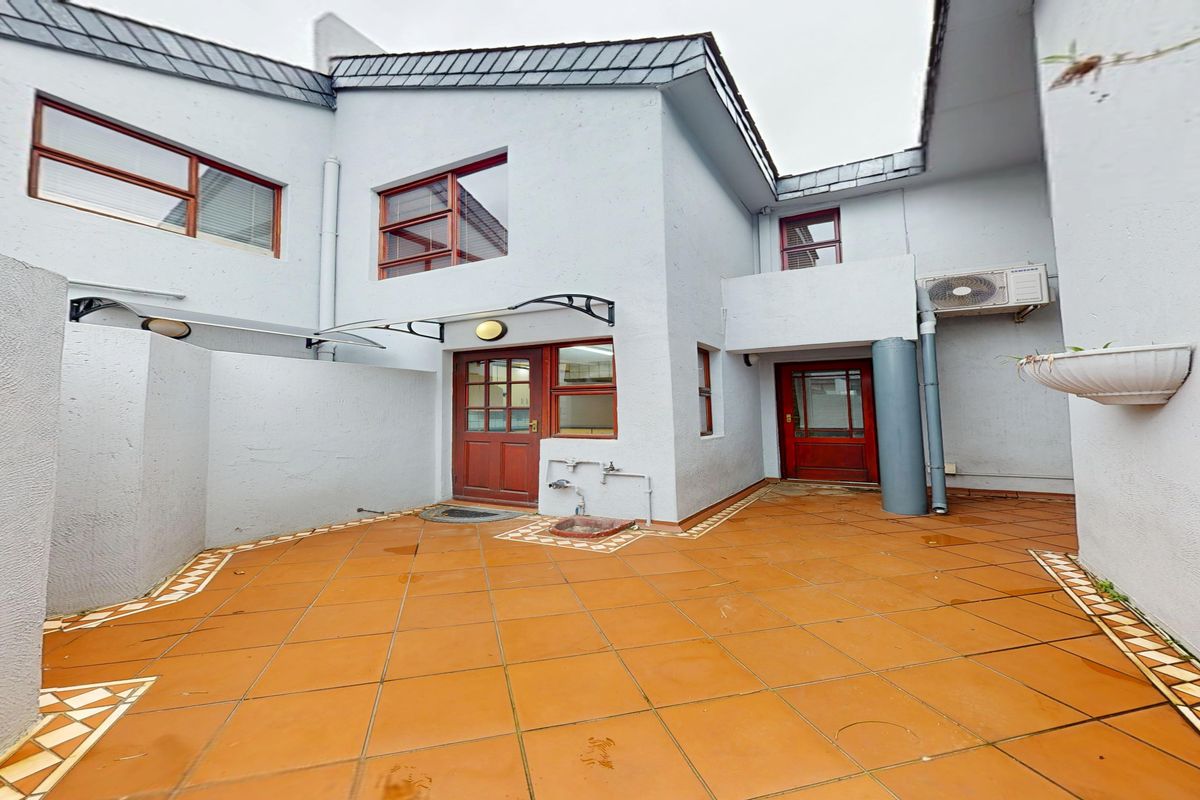 A private rear courtyard featuring tiled flooring, timber-framed access doors, and an external air conditioning unit, providing a functional outdoor space.
