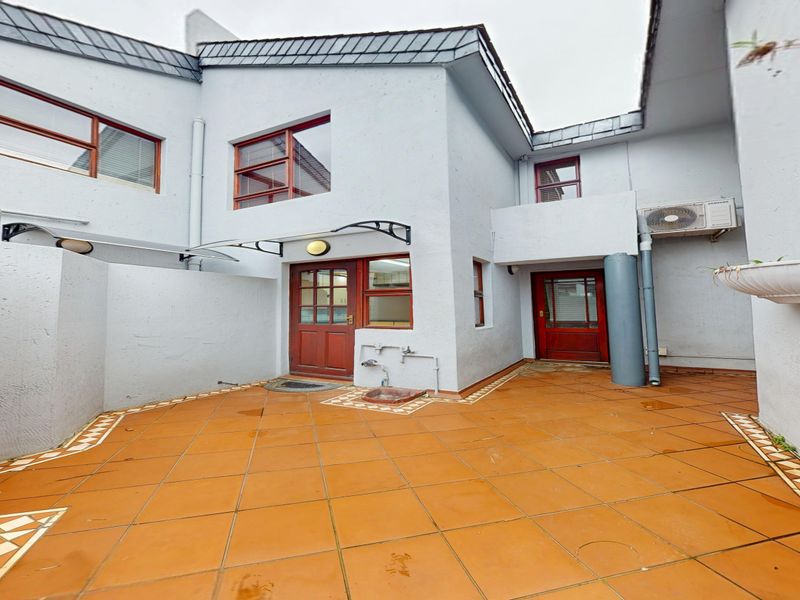 A private rear courtyard featuring tiled flooring, timber-framed access doors, and an external air conditioning unit, providing a functional outdoor space.