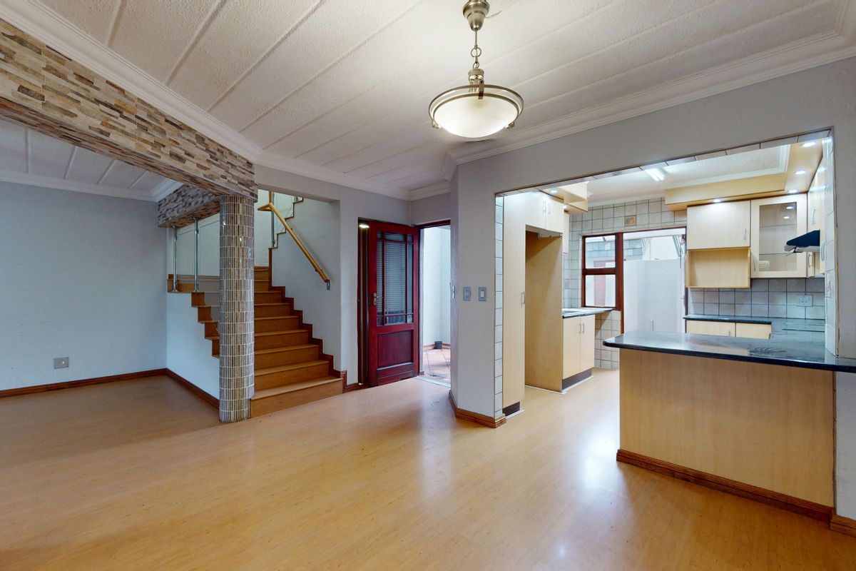 Open plan living area featuring laminate flooring, a wooden staircase with glass balustrade, and an adjoining kitchen with built-in cabinetry and breakfast bar.