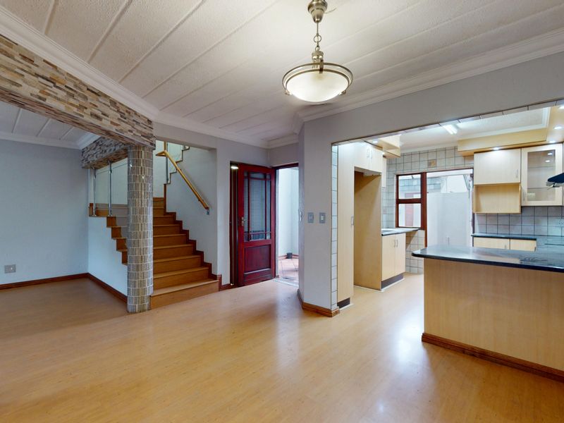 Open plan living area featuring laminate flooring, a wooden staircase with glass balustrade, and an adjoining kitchen with built-in cabinetry and breakfast bar.