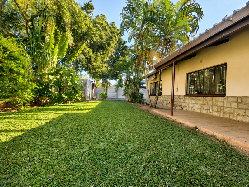 A well-maintained rear garden featuring a tiled patio, stone-clad exterior wall, and established greenery, providing a private outdoor living space.