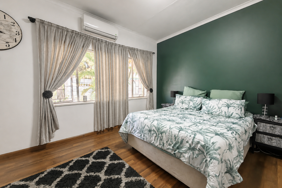 A well-maintained bedroom featuring timber flooring, a feature wall, and a wall-mounted air conditioning unit.