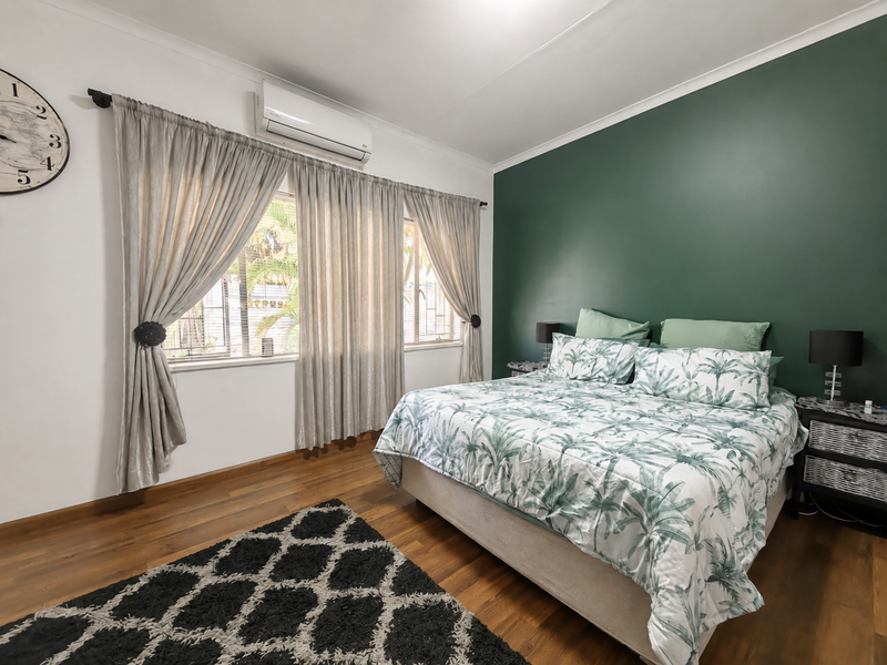A well-maintained bedroom featuring timber flooring, a feature wall, and a wall-mounted air conditioning unit.
