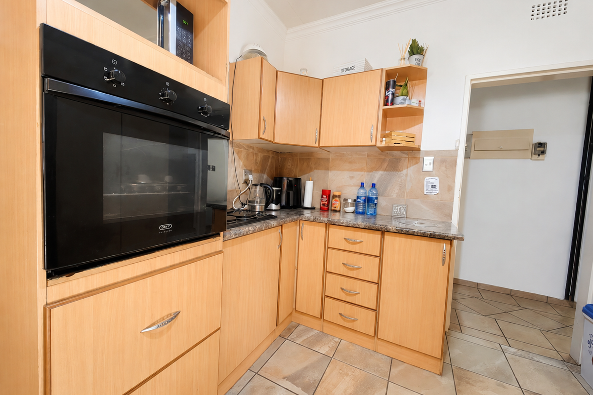 A functional kitchen featuring light wood-finish cabinetry, built-in oven, stone-look laminate countertops, and tiled flooring.