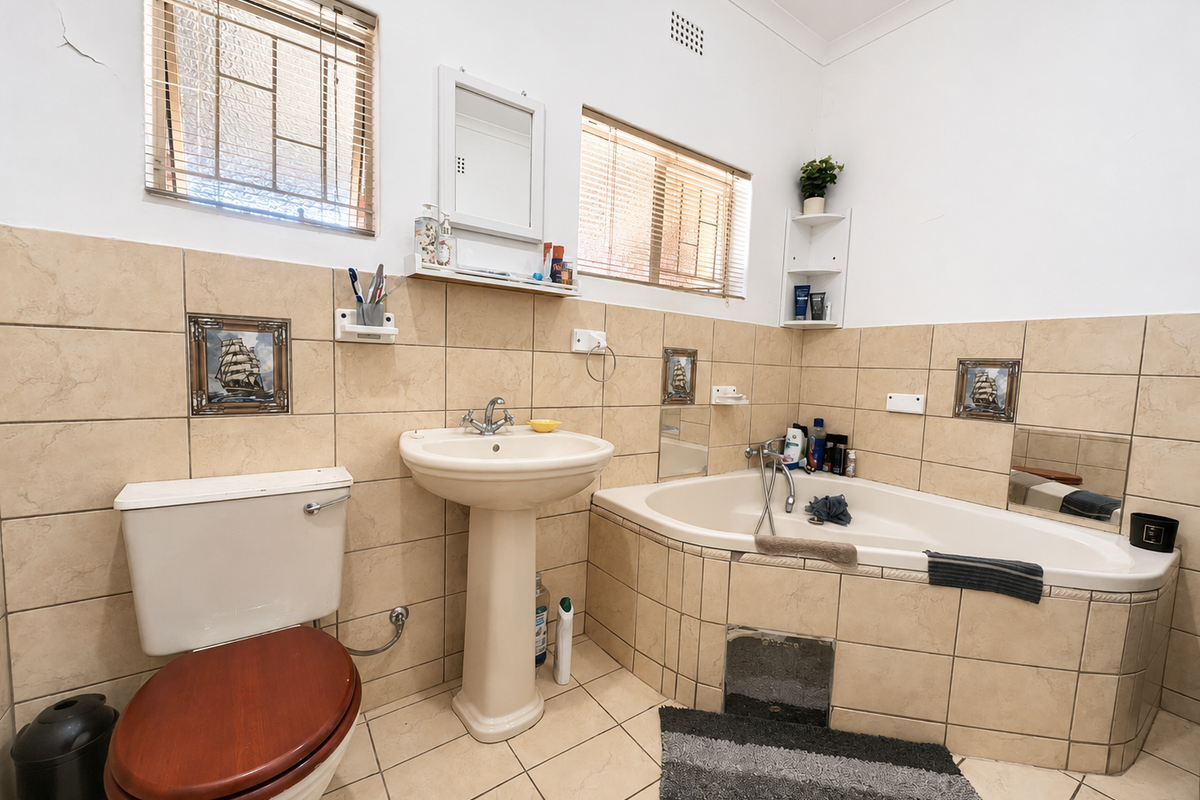 A functional bathroom featuring a pedestal basin, built-in bathtub, and tiled finishes, with natural light provided by two windows.