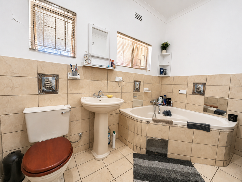 A functional bathroom featuring a pedestal basin, built-in bathtub, and tiled finishes, with natural light provided by two windows.
