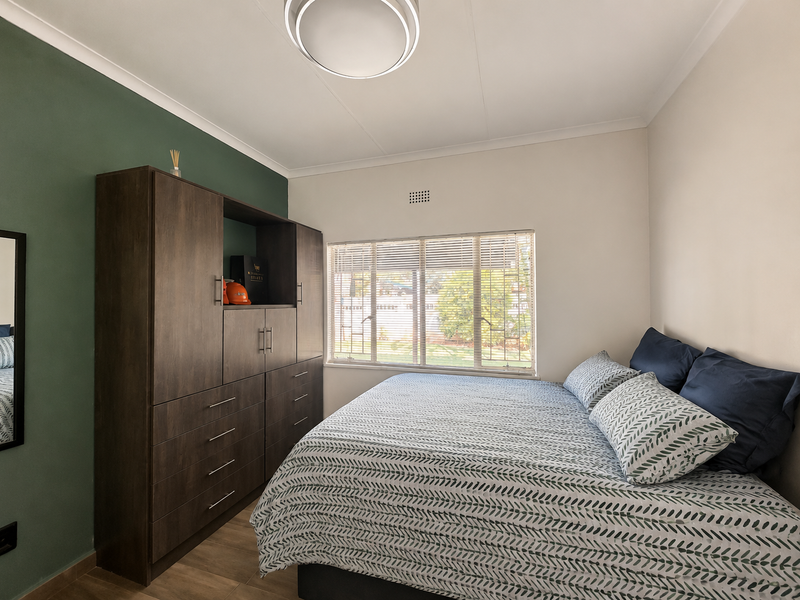 A well-maintained bedroom featuring a large built-in wardrobe, tiled flooring, and a window fitted with venetian blinds.