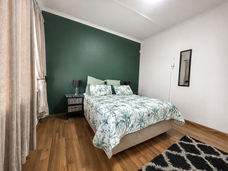 A well-maintained bedroom featuring laminate flooring, a bold green accent wall, and neutral white walls with classic cove cornicing.