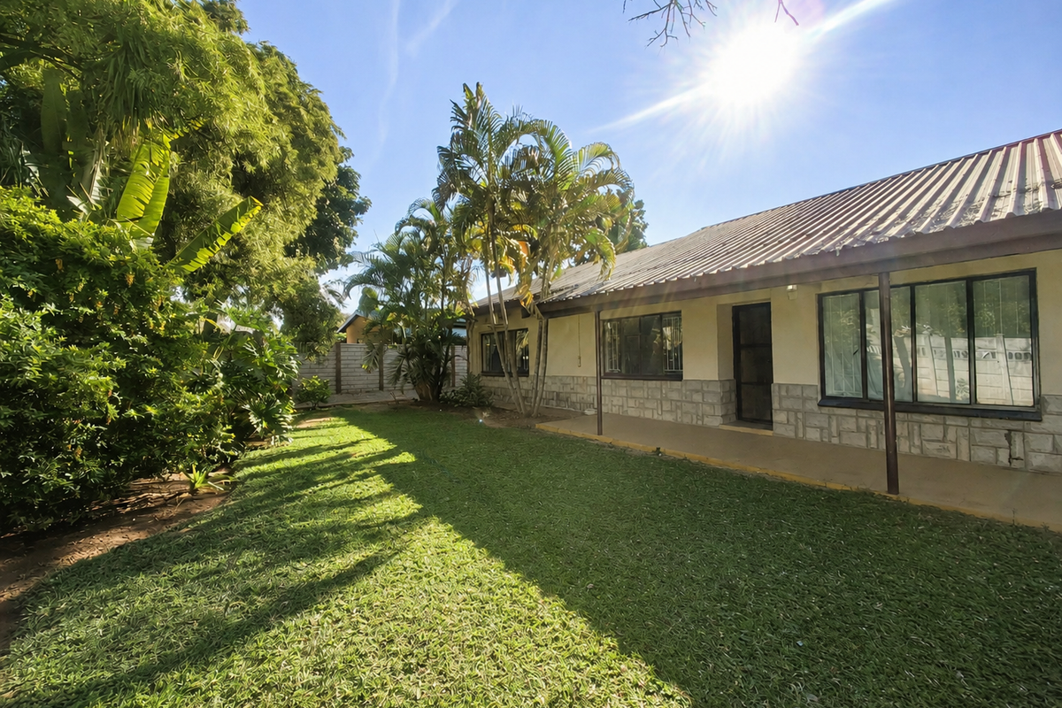 Rear view of the property featuring a covered patio, stone cladding, and a spacious garden area with established trees.