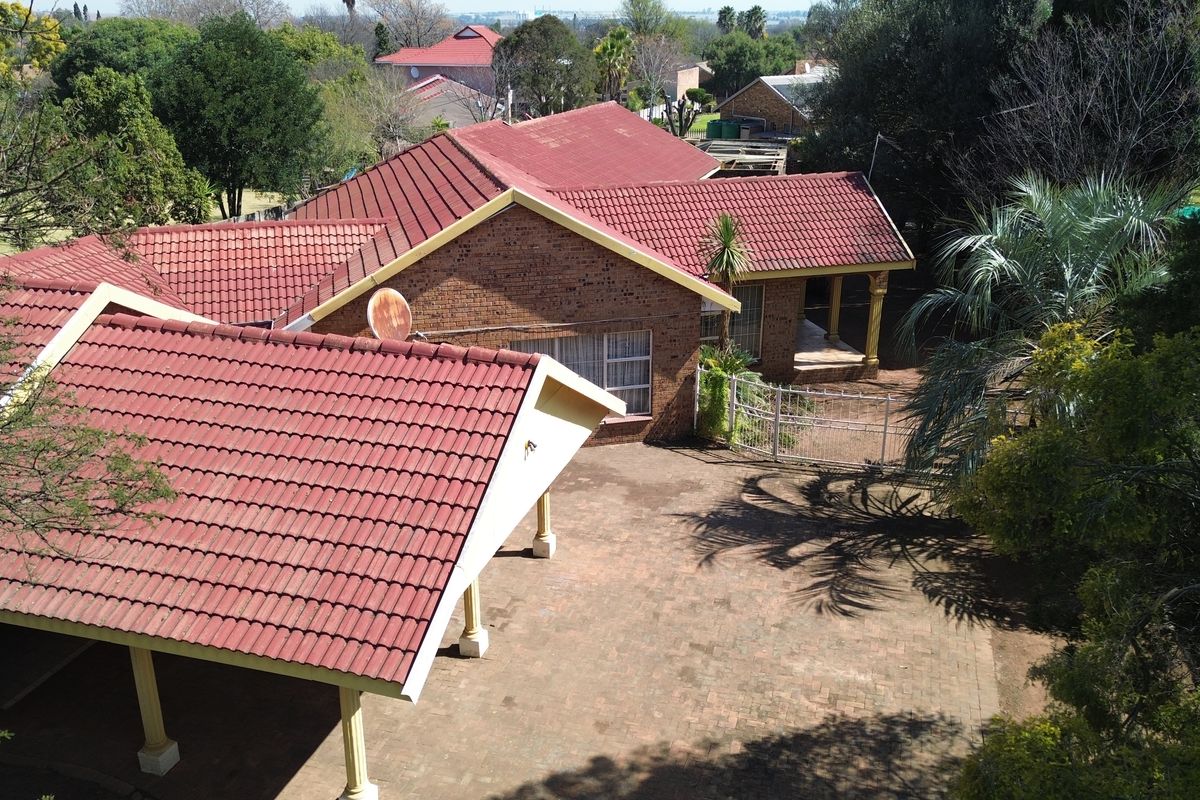 Aerial view of a residential property featuring a tiled roof, brick exterior, paved driveway, and a covered patio area.