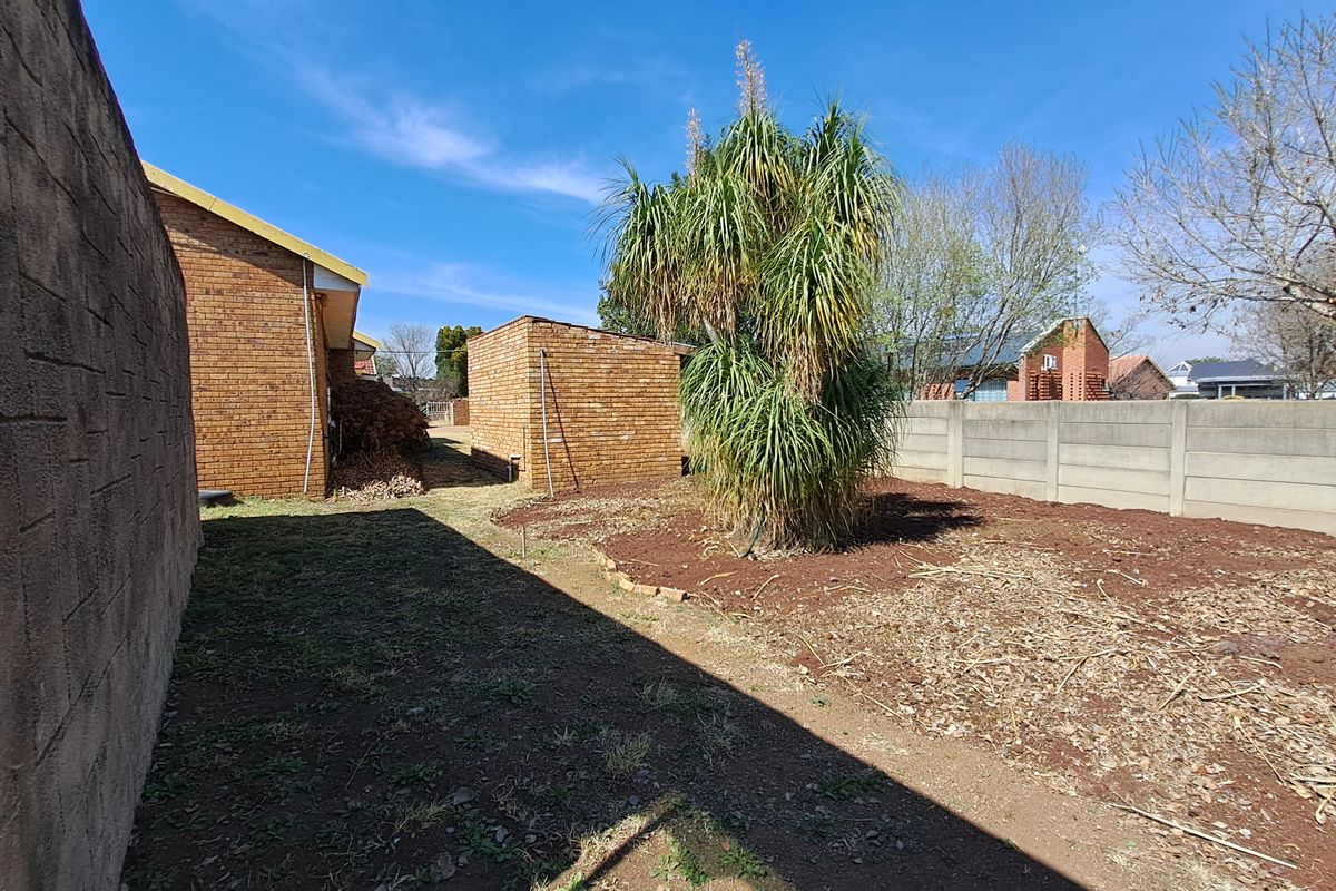 A rear exterior view of the property featuring a brick outbuilding, boundary walls, and an unlandscaped garden area with exposed soil.