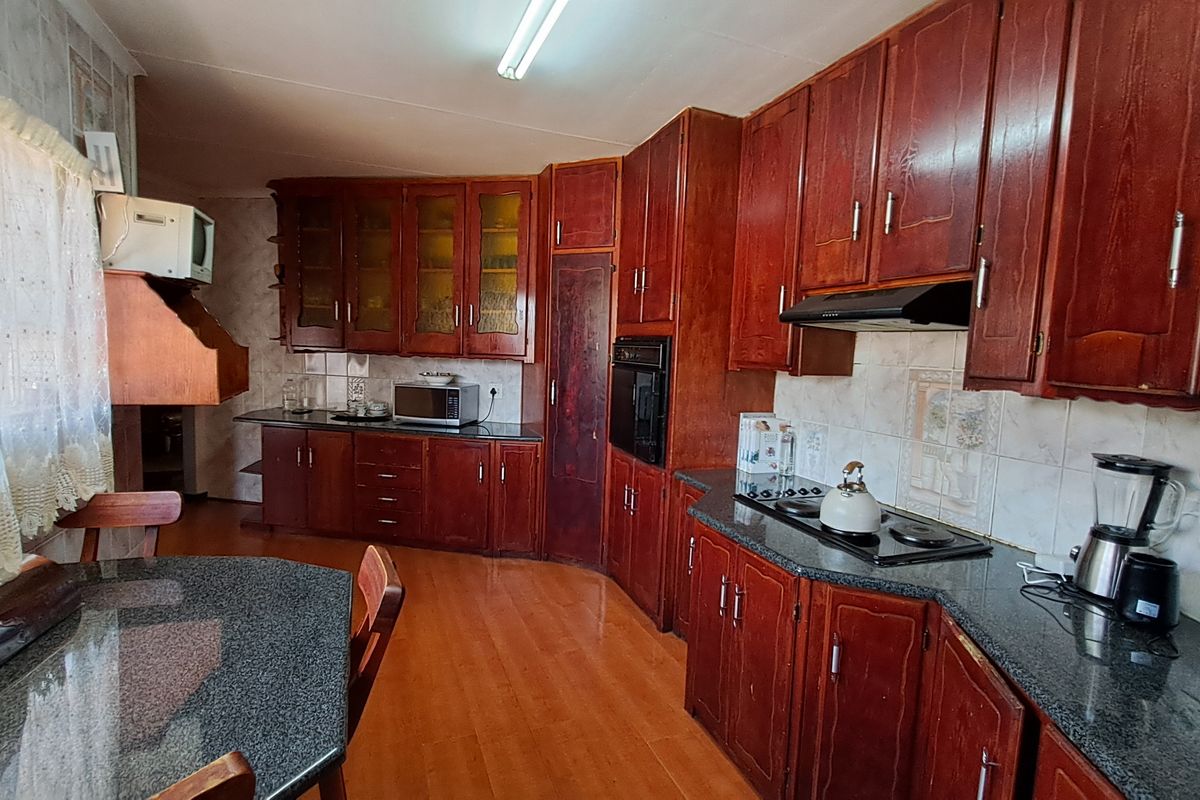 A functional kitchen featuring dark wood cabinetry, granite countertops, built-in oven, hob, and extractor fan with a tiled backsplash and laminate flooring.