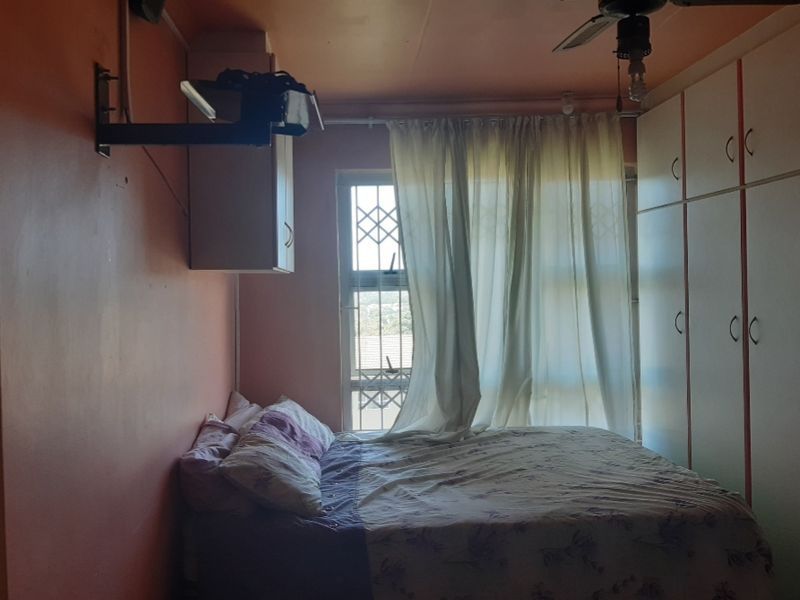 A bedroom featuring built-in cupboards, a ceiling fan, and a window with security bars, providing functional storage and ventilation.
