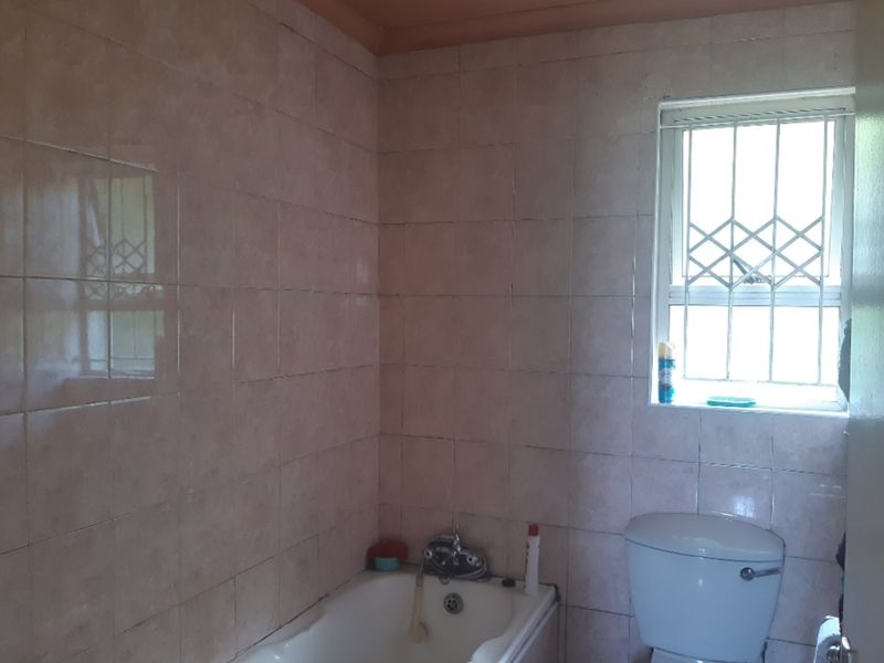 A functional bathroom featuring a bathtub, toilet, and full-height wall tiling with a security-fitted window.