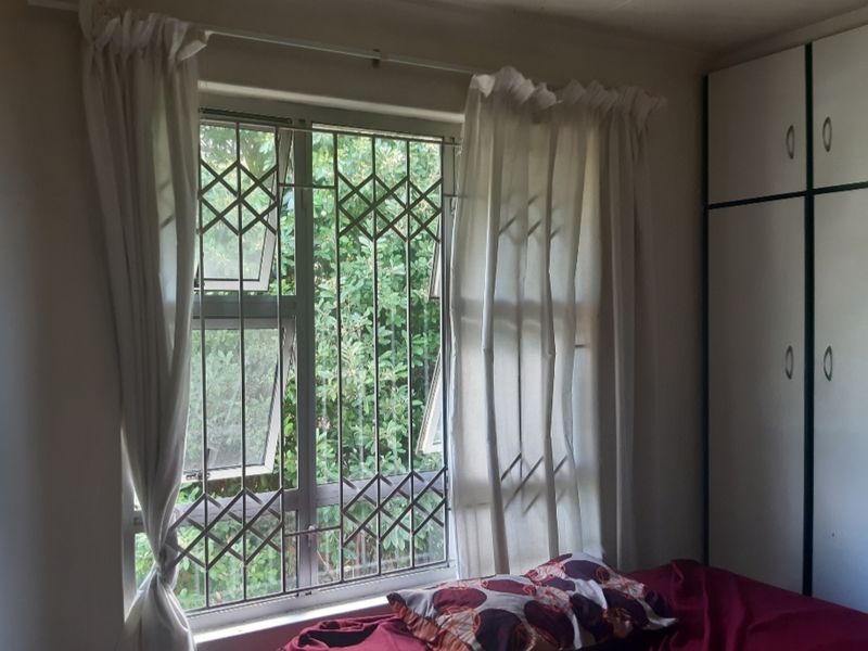 Bedroom featuring a built-in wardrobe and a window fitted with security burglar bars, offering a view of the surrounding greenery.