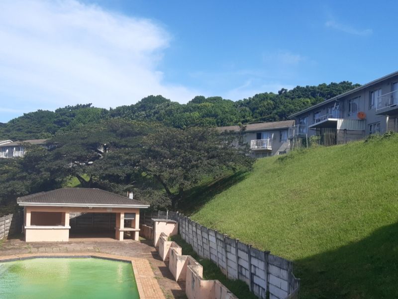 Exterior view of an apartment complex featuring a swimming pool, a communal poolside gazebo, and landscaped grassy slopes.