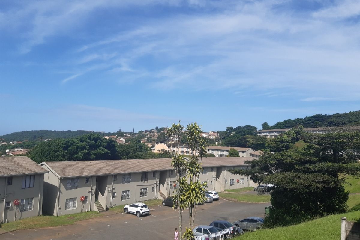 An elevated aerial view of the apartment complex, showcasing the building exterior, tiled roofing, and communal parking area.