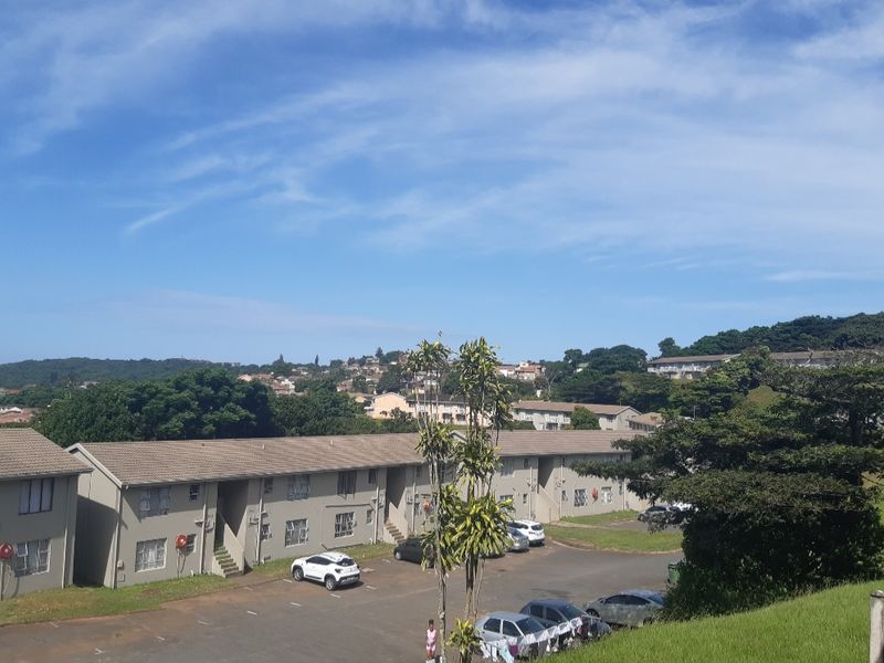 An elevated aerial view of the apartment complex, showcasing the building exterior, tiled roofing, and communal parking area.