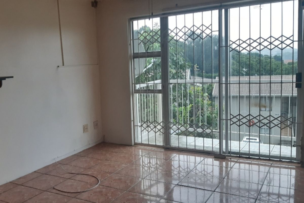 An empty living room featuring tiled flooring, a ceiling fan, and a sliding glass door with security gate access to a balcony.