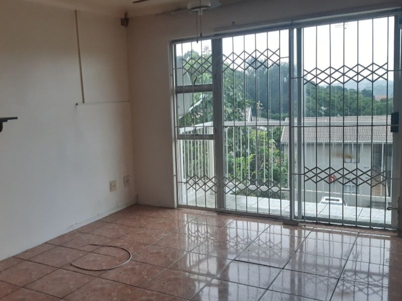 An empty living room featuring tiled flooring, a ceiling fan, and a sliding glass door with security gate access to a balcony.