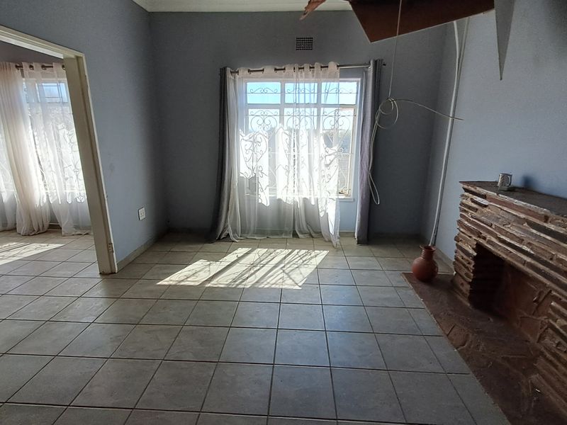 Spacious living area featuring ceramic floor tiles and a stone fireplace, requiring ceiling repairs and electrical maintenance.
