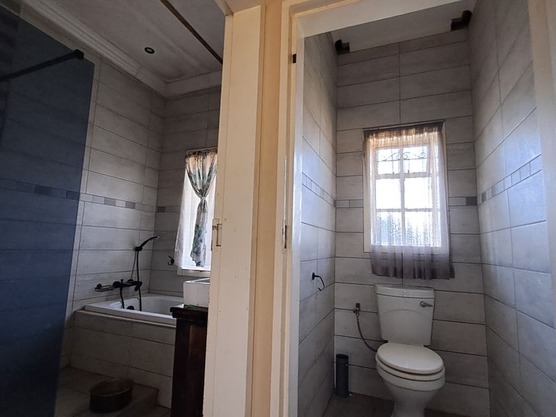 A functional bathroom featuring a built-in bathtub, separate shower enclosure, and toilet with neutral wall tiling throughout.