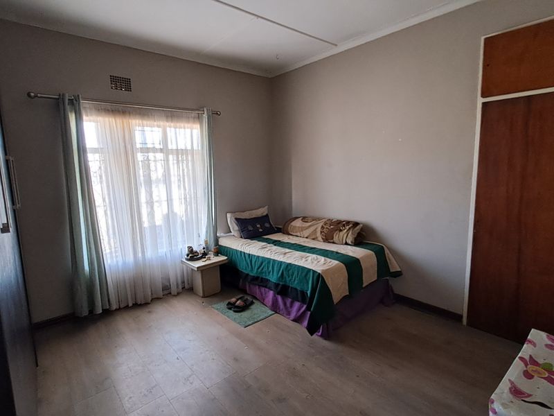 A bedroom featuring laminate flooring, a built-in wardrobe, and window security bars, requiring minor cosmetic updates to improve its overall condition.