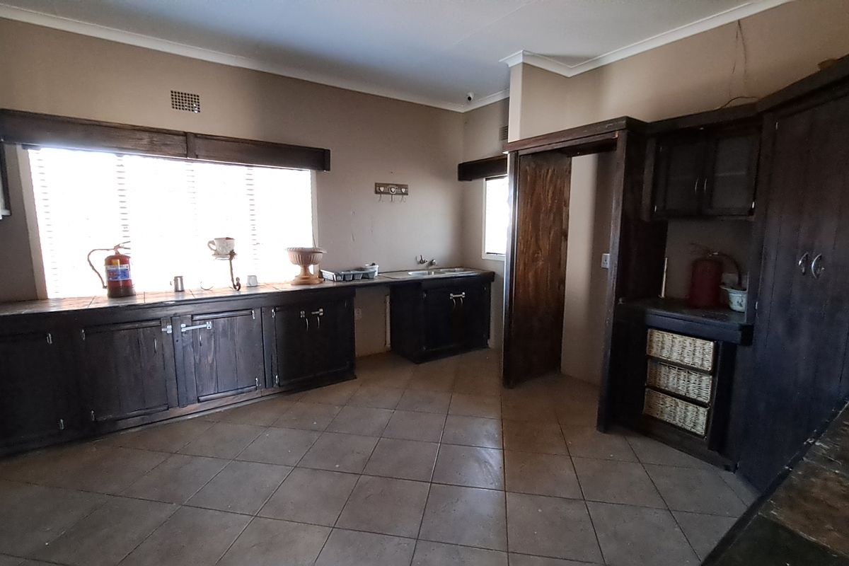 A spacious, empty kitchen featuring dark wood cabinetry, tiled flooring, and a functional sink area, offering significant potential for a modern renovation.