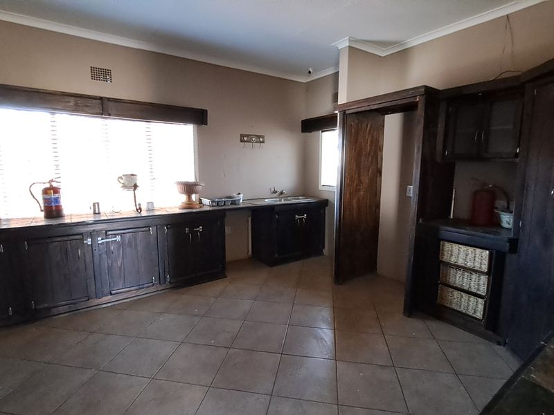 A spacious, empty kitchen featuring dark wood cabinetry, tiled flooring, and a functional sink area, offering significant potential for a modern renovation.