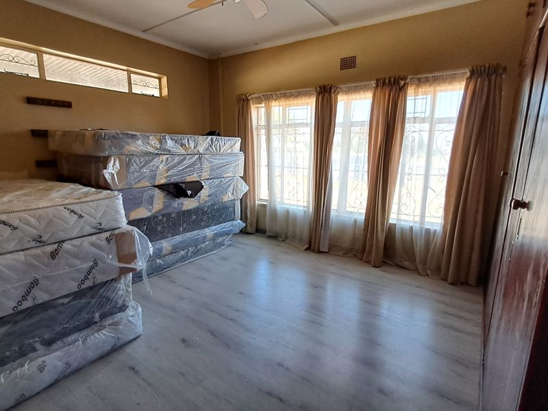 A spacious bedroom featuring light-toned laminate flooring, a built-in wardrobe, and large windows with security bars, offering a bright and functional living space.