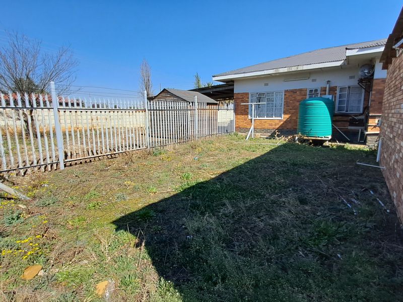 Rear exterior view of the property featuring a brick facade, metal security fencing, and a water storage tank set within a garden area.