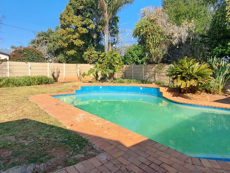 A backyard area featuring a swimming pool with brick coping, surrounded by a lawn and a precast concrete boundary wall.