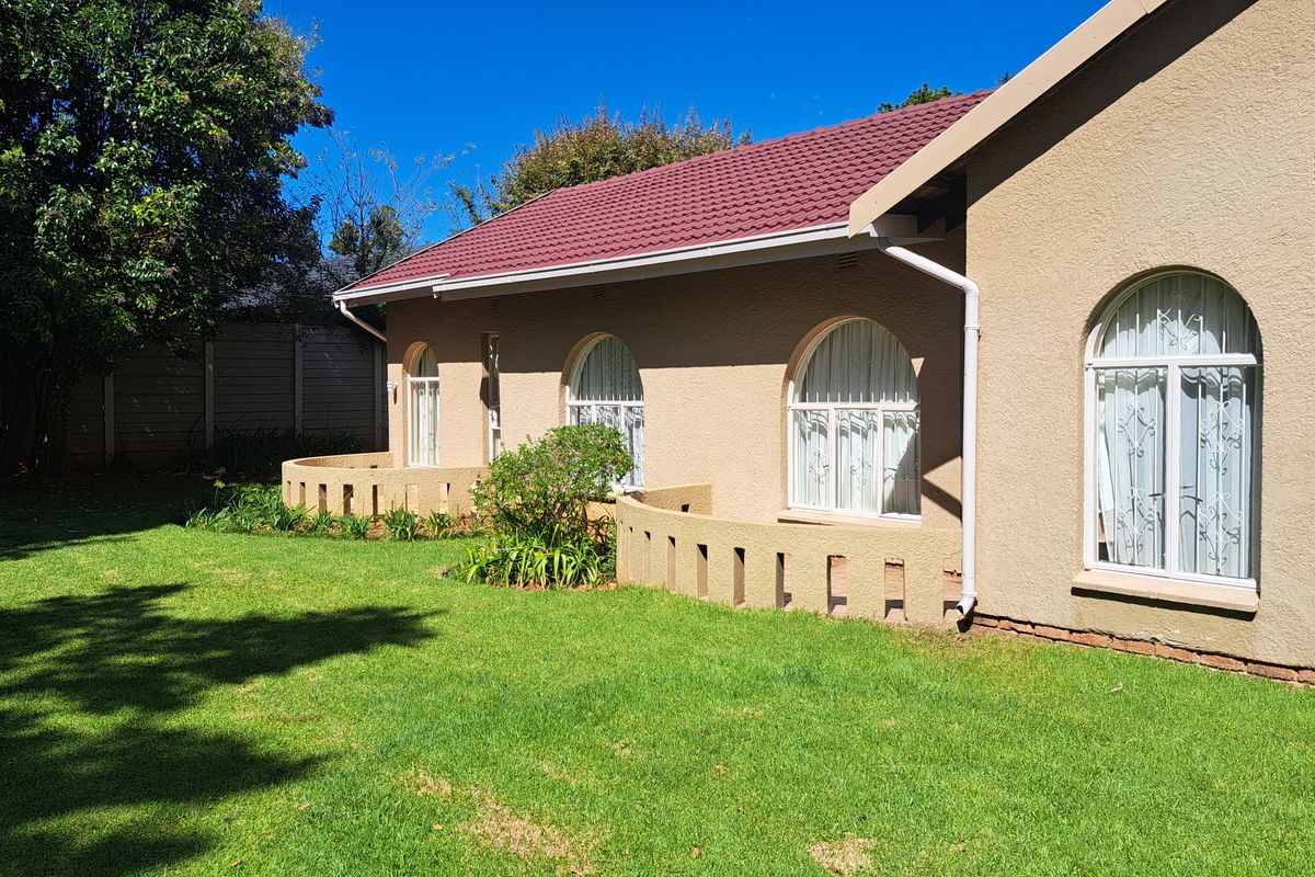 Rear view of the house featuring a tiled roof, arched windows with security bars, and low masonry garden walls set against a lawn.